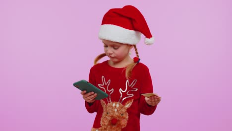 Girl-kid-in-Christmas-sweateruse-mobile-cell-phone,-plastic-credit-bank-cards,-win,-calebrate,-wow