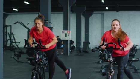 Athletic-women-group-riding-on-spinning-stationary-bike-training-routine-in-gym,-weight-loss-indoors