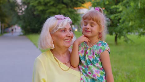 Little-granddaughter-child-embracing-kissing-with-her-grandmother-in-park,-happy-family-relationship