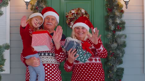 Senior-grandmother-grandfather-with-granddaughter-standing-at-Christmas-house-porch-waving-hello-hi