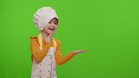 Child-girl-dressed-cook-chef-in-apron-pointing-at-right-on-blank-space-on-chroma-key-background