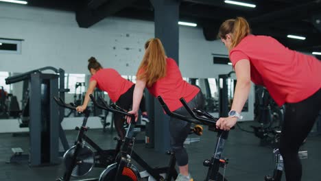 Healthy-Caucasian-group-of-women-exercising-workout-on-stationary-cycling-machine-bike-in-gym