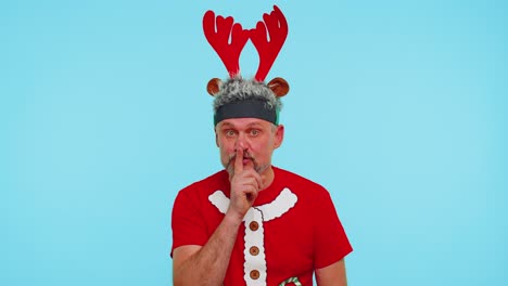 Man-wears-red-Christmas-t-shirt-presses-index-finger-to-lips-makes-silence-gesture-sign,-secret