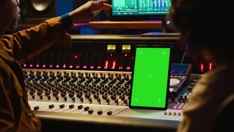 Diverse-music-experts-working-with-greenscreen-on-tablet-and-mixing-console