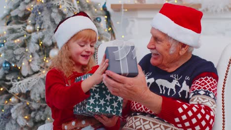Granddaughter-exhcanging-Christmas-gift-present-boxes-with-amazed-happy-elderly-grandfather-at-home