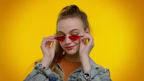 Seductive-cheerful-stylish-girl-in-denim-jacket-wearing-sunglasses,-charming-smile-on-yellow-wall