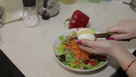 Female-hands-cut-an-egg-to-a-salad-with-red-bell-Pepper-and-lettuce-salad