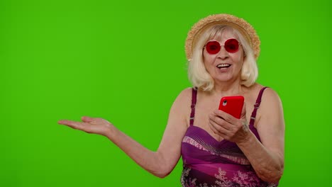 Senior-Rentnerin-Touristin-Im-Badeanzug-Zeigt-Hand-Zeigt-Werbeinhalte-Vom-Mobiltelefon