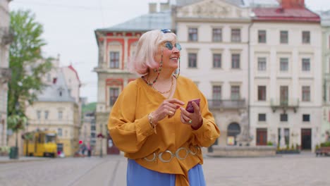 Anciana-Turista-Elegante-Que-Busca-La-Manera-De-Encontrar-Una-Ruta-Usando-Un-Teléfono-Inteligente-En-El-Casco-Antiguo-De-Lviv,-Ucrania