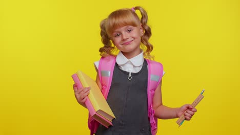 Cheerful-funny-schoolgirl-kid-with-books-dressed-in-uniform-wears-backpack-smiling-looking-at-camera