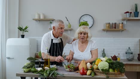 Elderly-grandparents-in-kitchen.-Funny-grandpa-joking-on-grandma.-Putting-a-lettuce-about-her-head