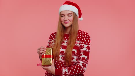 Cheerful-lovely-girl-in-sweater-Santa-hat-presenting-one-Christmas-box,-excited-by-holiday-gift
