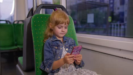 Young-little-child-girl-kid-in-city-train,-tram-or-bus-using-smartphone-chatting-with-friends