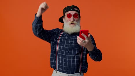 Elderly-bearded-man-use-mobile-phone-browsing-online-say-wow-yes,-big-win-news-doing-winner-gesture