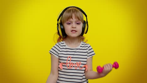 Child-girl-listening-music-via-headphones,-working-out-pumping-up-arm-muscles-lifting-pink-dumbbells
