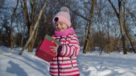 Fröhliches-Lächelndes-Mädchen-Blickt-Mit-Weihnachtsgeschenk-Geschenkbox-In-Die-Kamera-Im-Verschneiten-Winterpark