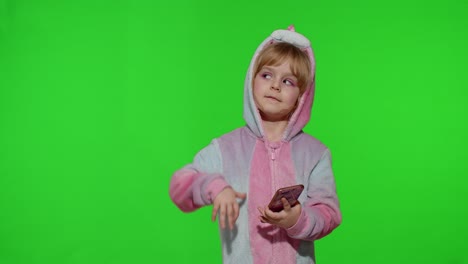 Kleines-Mädchen-Im-Einhorn-Pyjama-Benutzt-Smartphone,-Hält-Es,-Zeigt-Mit-Den-Händen-Auf-Etwas,-Kopiert-Platz