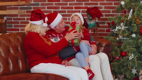 Grandfather,-grandmother-gifting-Christmas-present-box-to-amazed-happy-grandchild-girl-kid-at-home
