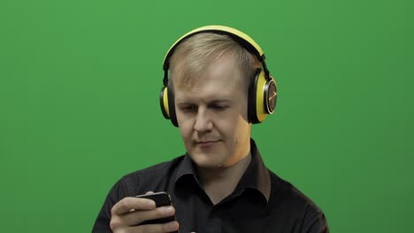 Guy-listens-to-music-in-wireless-yellow-headphones-and-dances.-Green-screen