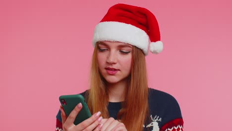 Frau-Im-Stilvollen-Weihnachtspullover-Schaut-Auf-Das-Smartphone-Display-Und-Freut-Sich-Aufrichtig-über-Den-Sieg,-Den-Erfolg-Und-Das-Glück
