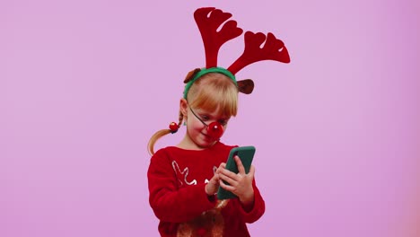 Girl-child-in-Christmas-deer-antlers-looking-smartphone-display-sincerely-rejoicing-win-success-luck