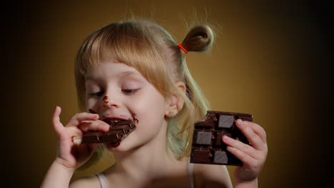 Happy-smiling-little-child-girl-kid-eating-milk-chocolate-bar-dessert-isolated-on-dark-background