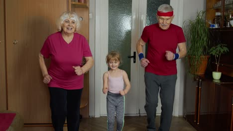 Granddaughter-and-mature-grandparents-in-sportswear-making-sports-jogging-workout-exercises-at-home