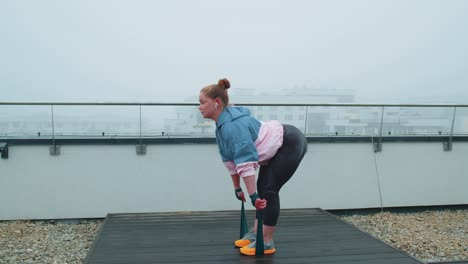 Sporty-girl-in-sportswear-does-yoga-stretching-exercising-using-rubber-band-on-roof-of-house-outdoor