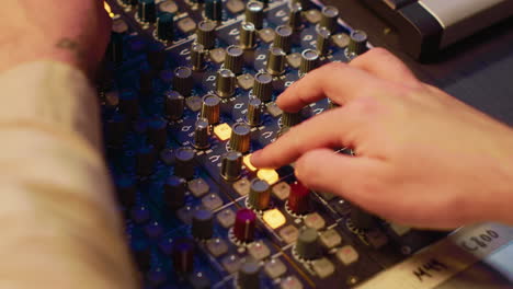 Audio-technician-twisting-pre-amp-knobs-and-buttons-on-board-in-control-room