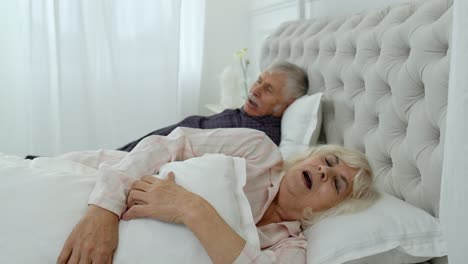 Senior-grandparents-couple-lying-and-sleeping-in-bed.-Woman-getting-disturbed-with-man-snoring
