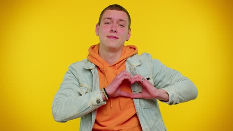 Smiling-teen-man-makes-heart-gesture-demonstrates-love-sign-expresses-good-feelings-and-sympathy