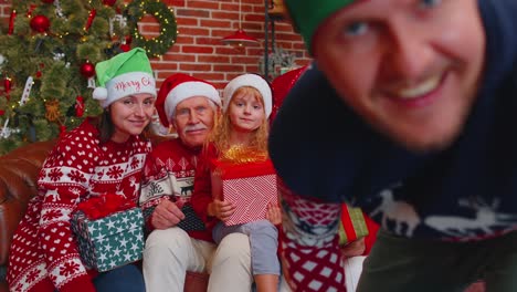 Man-sets-timer-on-mobile-phone-taking-multigenerational-family-selfie-portrait-celebrating-Christmas