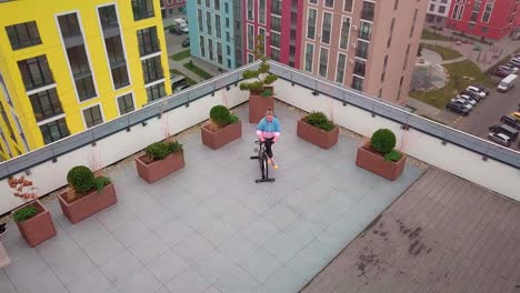 Healthy-Caucasian-woman-exercising-workout-on-stationary-cycling-machine-bike-on-house-rooftop-gym