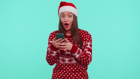 Junges-Teenager-Mädchen-Im-Weihnachtspullover-Schaut-Auf-Smartphone-Display-Und-Freut-Sich-Aufrichtig-über-Erfolg-Und-Glück