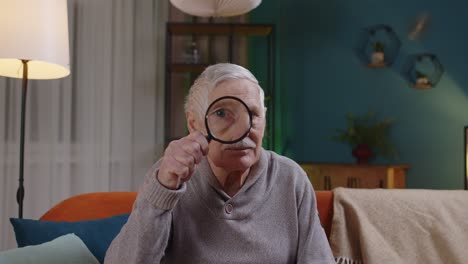 Senior-grandfather-man-looking-through-magnifying-glass,-reading,-researching,-examining-at-home