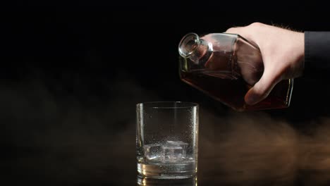 Barmann-Gießt-Whisky-Cognac-Brandy-Aus-Der-Flasche-In-Trinkglas-Mit-Eiswürfeln-Auf-Dunklem-Hintergrund