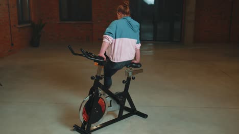 Athletic-girl-make-acrobatic-trick-on-bike-exercising-workout-on-stationary-cycling-machine-indoors
