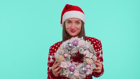 Adult-smiling-girl-in-red-Christmas-holiday-sweater-hold-raise-point-finger-on-festive-wreath-toy