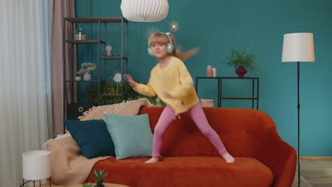 Happy-child-girl-kid-in-headphones-dancing-and-jumping-while-listening-to-the-music-at-home-alone