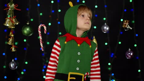 Kid-girl-in-Christmas-elf-Santa-Claus-helper-costume-holding-finger-near-lips-for-silence,-hush-sign