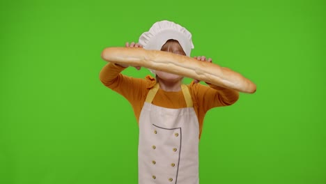 Child-girl-dressed-in-apron-like-chef-cook-baker-breaking-and-eating-fresh-baguette-on-chroma-key