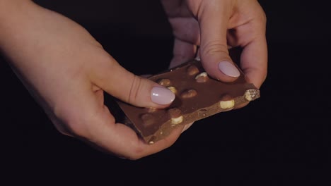 Woman-breaks-black-chocolate-bar-with-nuts.-Close-up.-Slow-motion
