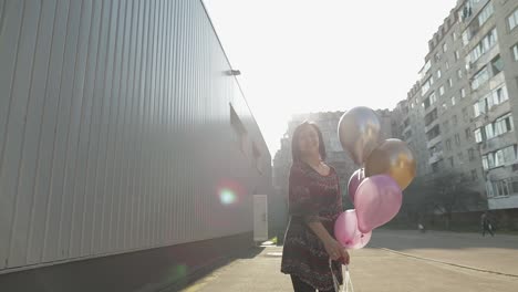 Pretty-woman-in-dress-holding-balloons-with-helium-outdoors-in-daylight