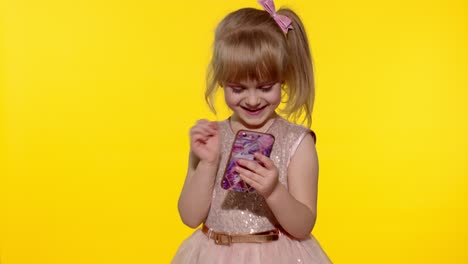 Child-girl-in-dress-using-mobile-cell-phone,-found-out-great-big-win-news.-Kid-doing-winner-gesture
