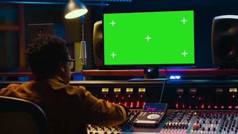 Audio-technician-works-on-music-post-production-with-greenscreen-in-control-room