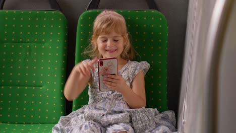 Child-girl-in-city-bus-or-tram-transport-use-mobile-cell-phone-sincerely-rejoicing-win,-good-news