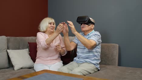 Senior-man-playing-game-in-virtual-reality-headset-glasses,-woman-laughing-with-him-action-at-home