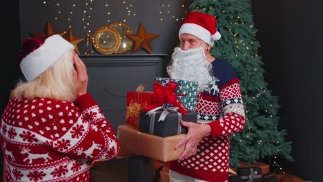 Grandfather-Santa-Claus-gifting-Christmas-present-box-to-surprised-grandmother,-senior-couple-family
