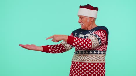 Grandfather-in-Santa-Christmas-sweater-showing-thumbs-up-and-pointing-empty-place,-advertising-area
