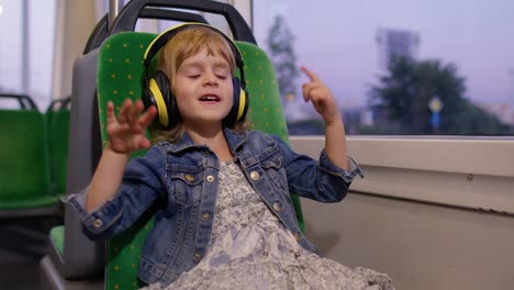 Little-child-girl-wearing-headphones-listening-music,-relax-dancing-while-traveling-by-bus-in-city